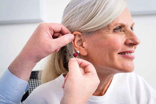 Ältere Frau bekommt ein modernes Hörgerät eingesetzt, Hörakustik und Hörgeräteberatung.